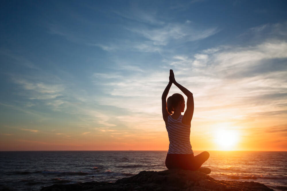 Frau macht Yoga am Meer bei Sonnenuntergang