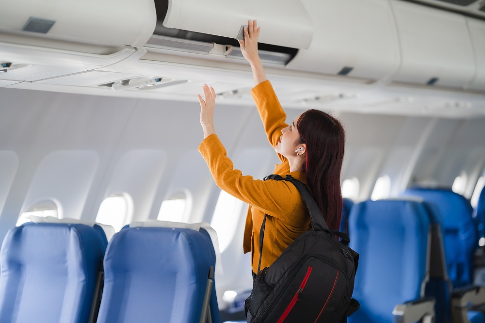 Frau verstaut Gepäck im Flugzeuggepäckfach