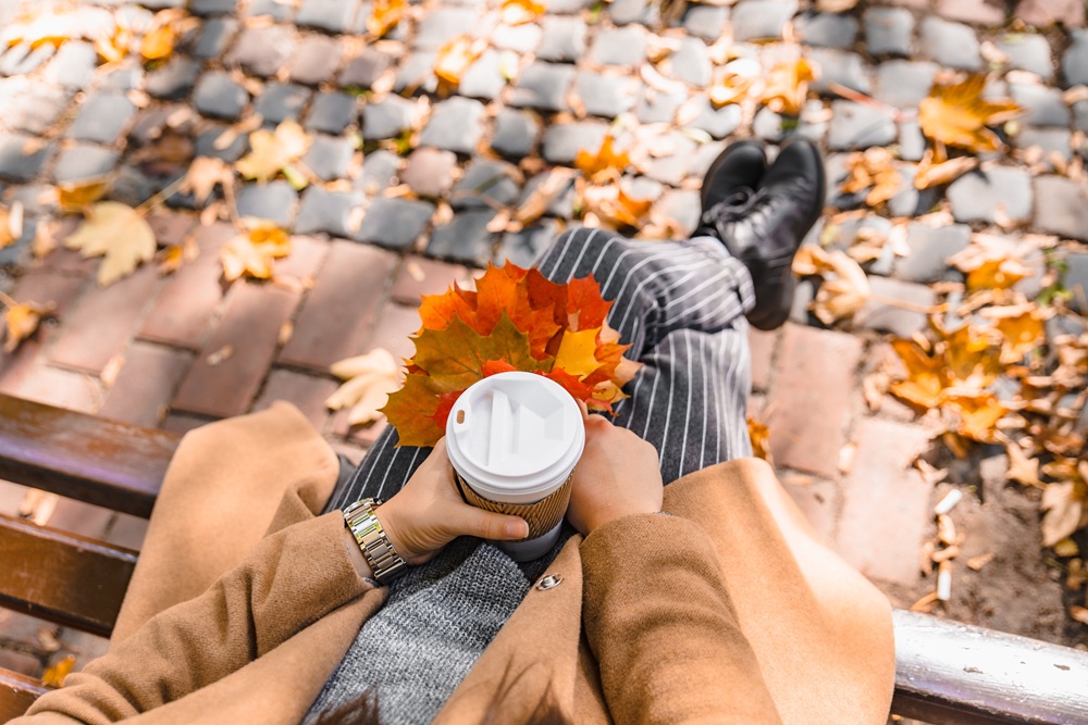 frau mit kaffee to go auf einer Bank