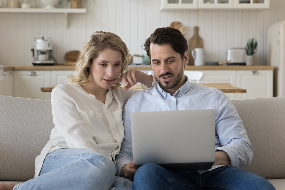 Nettes Paar auf dem Sofa zuhause schaut in den Laptop und überlegt